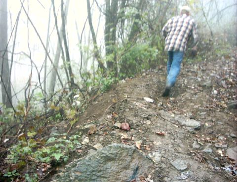 1990 Ford Bronco - A person walks up a steep, muddy hill in a wooded area.