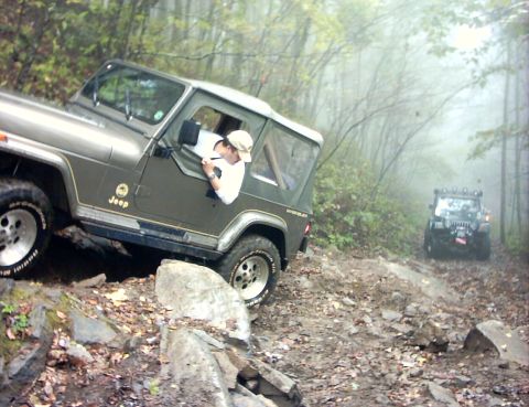 1990 Ford Bronco - Two Jeeps navigate a challenging, rocky trail through a misty forest.