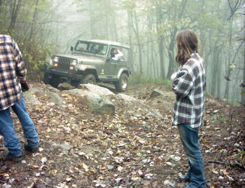 1990 Ford Bronco - A Jeep Wrangler navigates a challenging off-road path in a foggy forest environment.