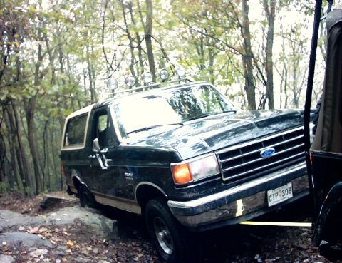 1990 Ford Bronco - A Ford Bronco navigates a challenging, wooded off-road path with another vehicle close by.
