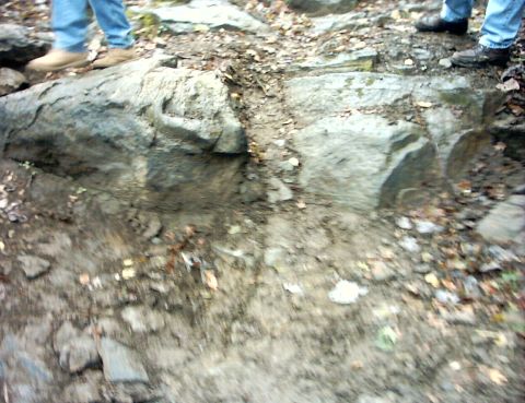 1990 Ford Bronco - A off-road scene with large rocks and the legs of individuals navigating the challenging terrain.