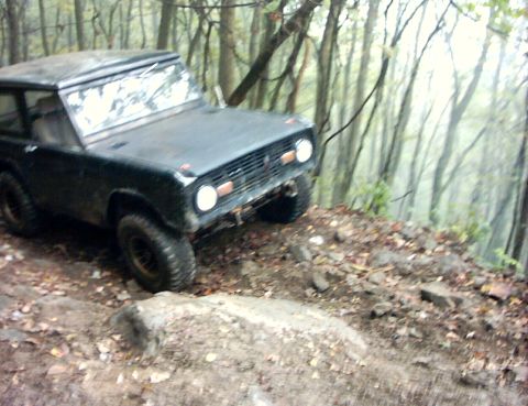 1990 Ford Bronco - A classic Ford Bronco navigates a challenging off-road path through a dense forest.