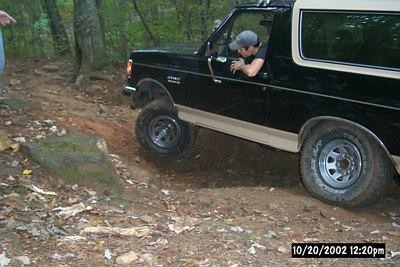 1990 Ford Bronco - A driver navigates a black Ford Bronco through a wooded, off-road trail.