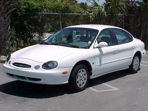 White Ford Taurus sedan parked in a lot, front three-quarter view with palm trees behind