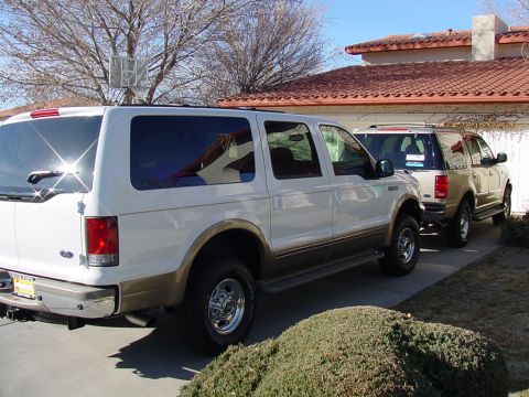 2002 Ford Excursion - Two large SUVs are parked in a driveway in front of a house.