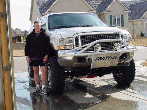 2002 Ford Excursion - A white 2002 Ford Excursion is shown with a custom front bumper and large off-road tires, parked in a driveway.