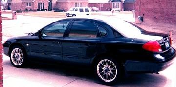 2000 Ford Taurus - Side profile of a black 2000 Ford Taurus sedan with aftermarket wheels.