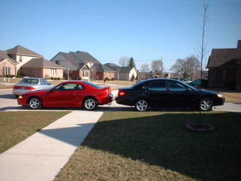 2000 Ford Taurus - A black 2000 Ford Taurus sedan is parked on the street next to a red coupe.