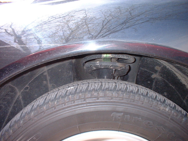 Close-up of Firestone tire and coil spring visible in wheel well of a dark sedan fender