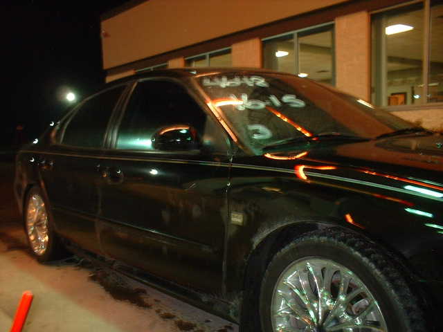 Black sedan parked at night, side view. Writing on windshield