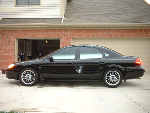 Black Ford Taurus sedan, side profile, on chrome wheels in front of garage
