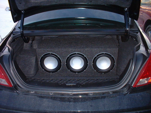 Open trunk with three subwoofers in carpeted box, raised parcel shelf above
