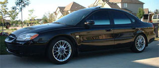 2000 Ford Taurus - A black 2000 Ford Taurus is parked in a suburban driveway on a sunny day.