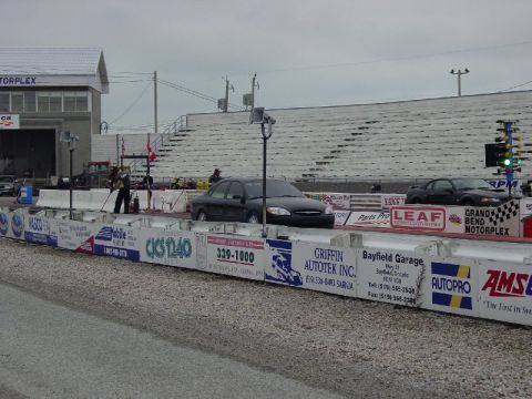 2000 Ford Taurus - A black 2000 Ford Taurus is positioned at the starting line of a drag strip, with another car visible further down the track.