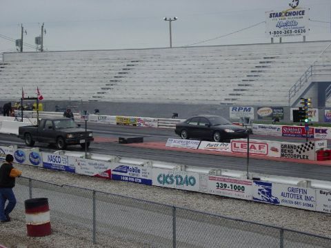 2000 Ford Taurus - A drag race is underway with a truck and a sedan on the track, under a cloudy sky.