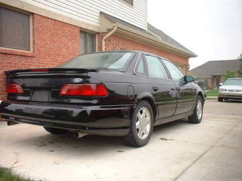 2000 Ford Taurus - A black 2000 Ford Taurus is parked in a driveway next to a house, with another car visible in the background.