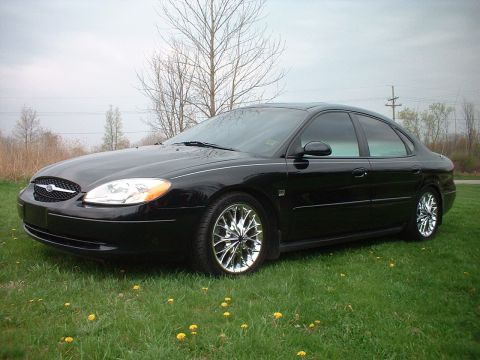 2000 Ford Taurus - A black 2000 Ford Taurus sedan is shown from a three-quarter front view, parked on a grassy area with trees in the background.
