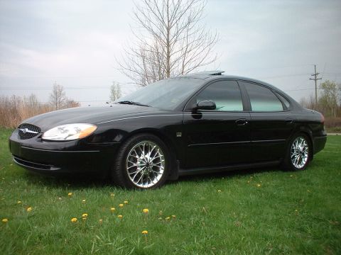 2000 Ford Taurus - A black 2000 Ford Taurus sedan with custom chrome wheels is shown from a three-quarter front view.