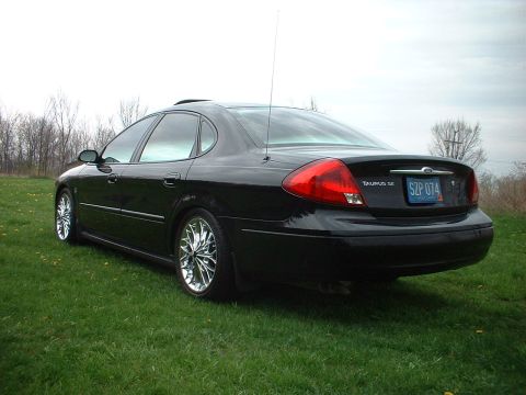 2000 Ford Taurus - A black 2000 Ford Taurus is parked on a grassy field with trees in the background.