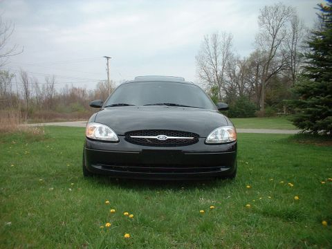 2000 Ford Taurus - A black 2000 Ford Taurus is shown from the front, parked in a grassy area with trees in the background.