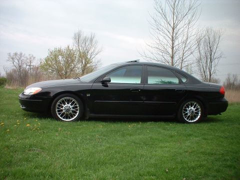 2000 Ford Taurus - A black sedan is parked on a grassy area with trees in the background under an overcast sky.