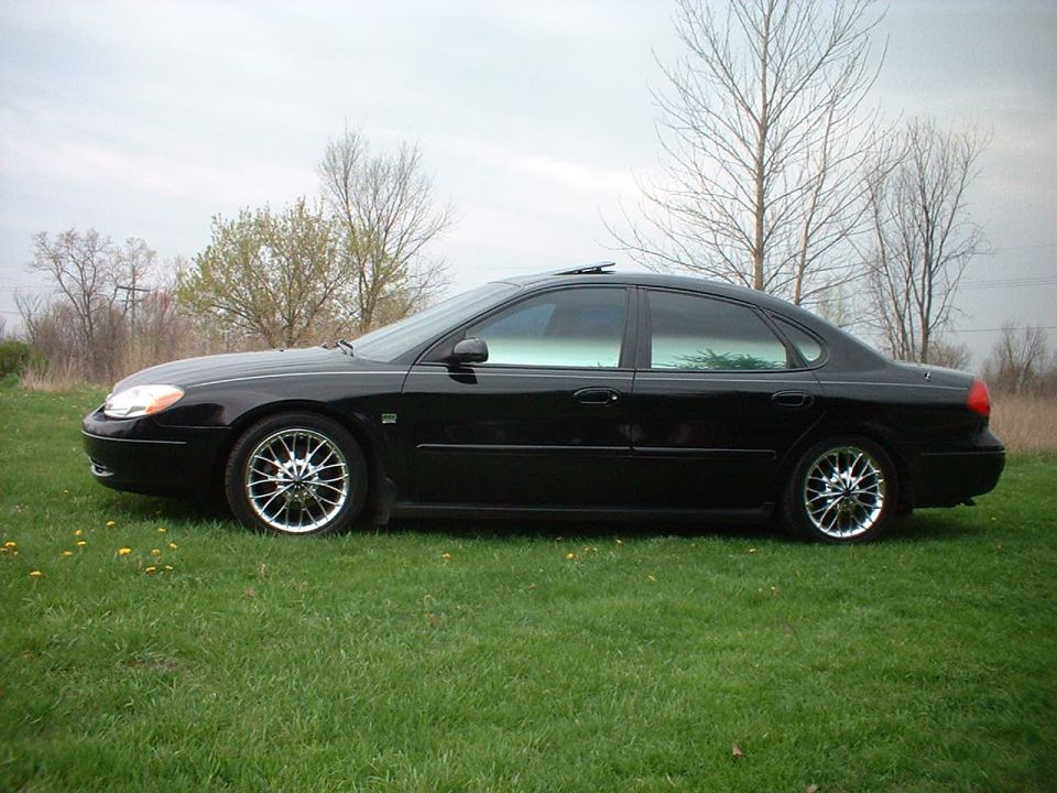 Black sedan parked on grass, side view. Looks like a Ford Taurus, but not a 2000 model