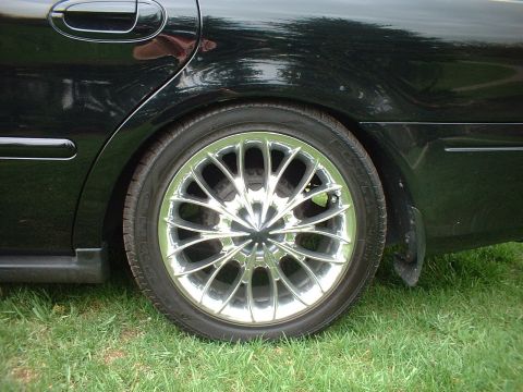 2000 Ford Taurus - A black sedan's rear wheel and side panel are visible, with grass in the background and a watermark at the bottom right.