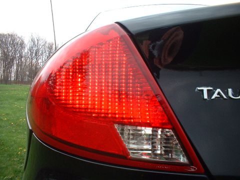 2000 Ford Taurus - The rear of a black sedan is shown with a prominent red taillight and partial badging.