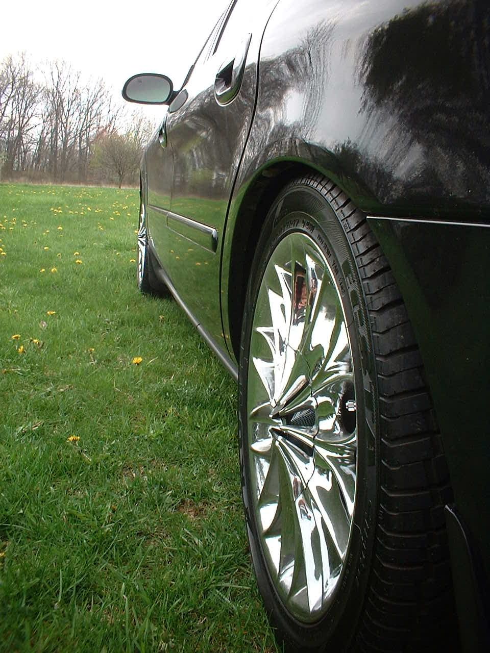 Black sedan side view, chrome wheel, grassy field with trees in background