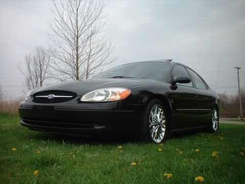 2000 Ford Taurus - A black 2000 Ford Taurus sedan with custom chrome wheels is shown from a low angle in a grassy area.