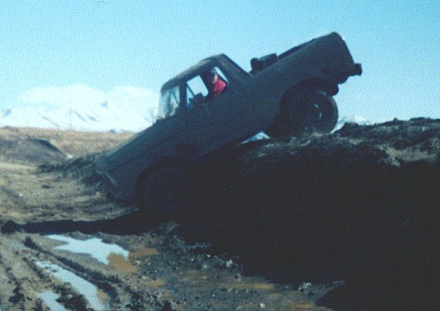 Full-size SUV nose-down over a steep dirt bank into a muddy pit off-road