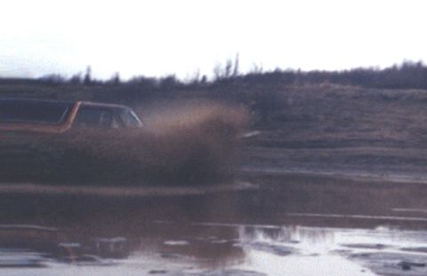 1978 Ford Bronco - An orange SUV drives through a water-filled track, creating a large splash.