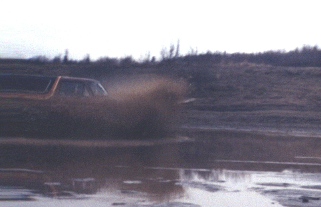 Brown SUV blasting through a mud puddle and throwing a big spray of muddy water