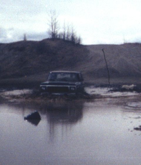 1978 Ford Bronco - A dark 1978 Ford Bronco navigates a muddy terrain, with its reflection visible in the water.