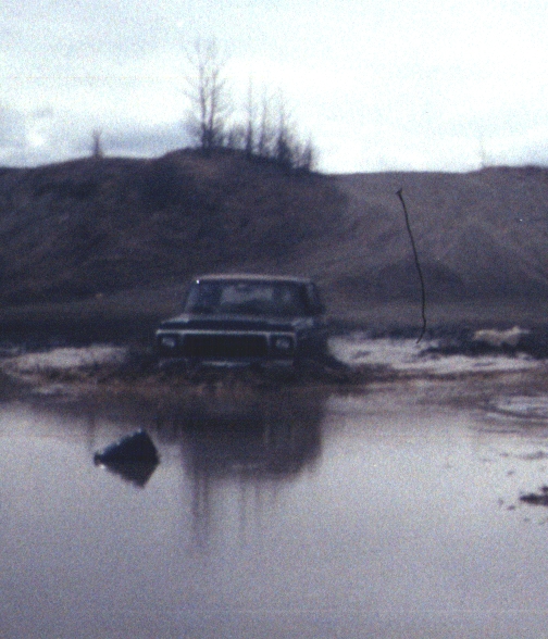 Dark Ford truck sitting in a large muddy water hole with reflection in the water