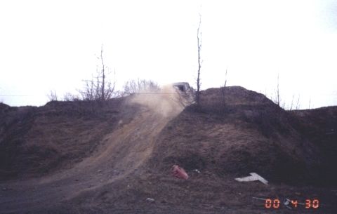 1978 Ford Bronco - A white SUV navigates a steep dirt incline, creating a cloud of dust as it ascends.