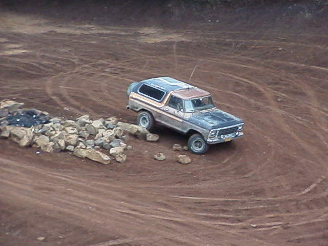 1978 Ford Bronco driving on a dirt track with rocks