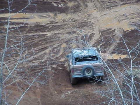 1978 Ford Bronco - A 1978 Ford Bronco navigates a steep, muddy incline, with a spare tire visible on the back.