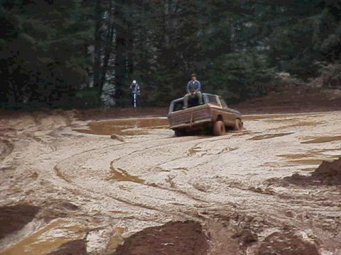 1978 Ford Bronco - A 1978 Ford Bronco navigates a muddy terrain, with one person seated on its tailgate.
