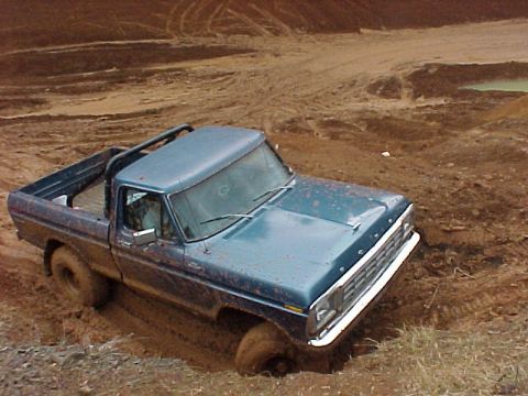 1978 Ford Bronco - A blue pickup truck is stuck in thick mud on an off-road trail.