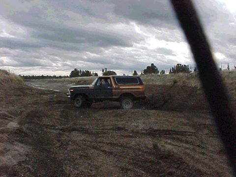 1978 Ford Bronco - This two-tone 1978 Ford Bronco navigates a rough, muddy terrain under a dramatic, cloudy sky.