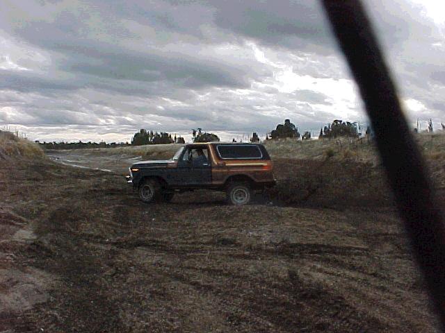 1978 Ford Bronco in brown and black driving on a dirt track under a cloudy sky