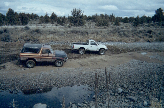 1978 Ford Bronco parked next to a white pickup truck on a dirt road