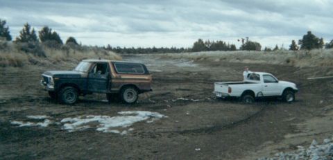 1978 Ford Bronco - A Bronco is being pulled out of the mud by a pickup truck under a cloudy sky.