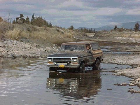 1978 Ford Bronco - A 1978 Ford Bronco navigates a rocky stream bed under a cloudy sky.