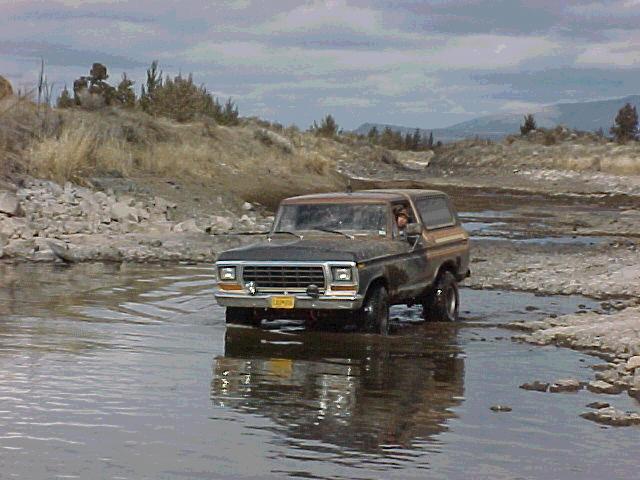Brown 1978 Ford Bronco driving through shallow water, front-right quarter view