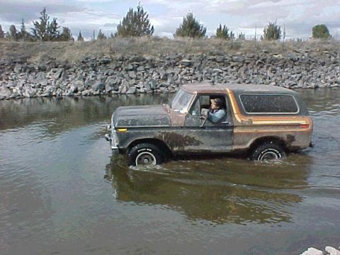 1978 Ford Bronco - A person drives a 1978 Ford Bronco through a rocky stream under a cloudy sky.