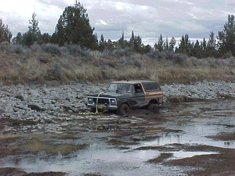 1978 Ford Bronco - A 1978 Ford Bronco is stuck in a muddy, rocky area with trees in the background.