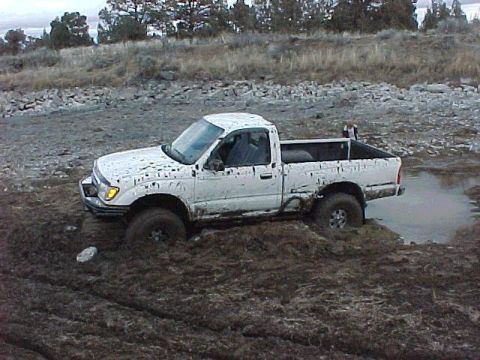 1978 Ford Bronco - A white pickup truck is stuck in thick mud, with its tires partially submerged.