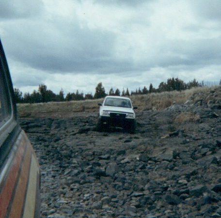 1978 Ford Bronco - A white SUV navigates a rough, rocky landscape under a cloudy sky.